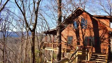 A log cabin with a wooden deck and a staircase leading to the entrance.