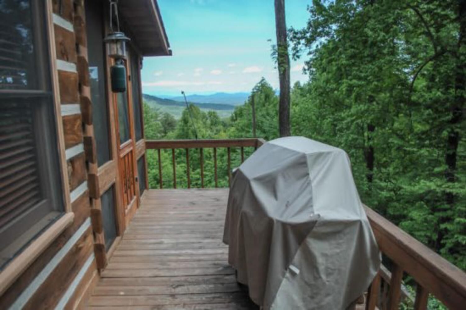 A wooden deck with a covered grill, overlooking a forested area with distant mountains.