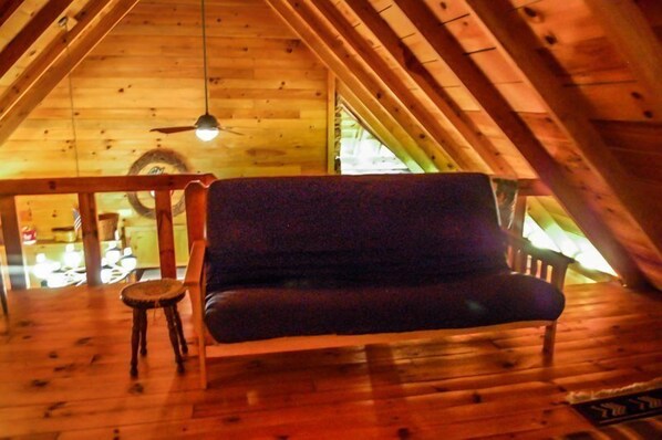 A cozy attic room with a wooden floor, a dark sofa, a small round table, and a ceiling fan. - Bear Lake Lodge (Blue Ridge)