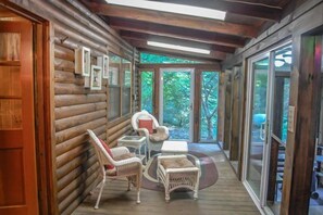 L’intérieur d’une cabane en rondins, avec un plafond en bois, une porte vitrée donnant sur l’extérieur, des meubles en osier et des tableaux encadrés accrochés au mur.