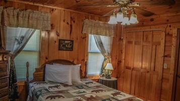 A wooden cabin bedroom with a bed, a nightstand, a lamp, and a ceiling fan.