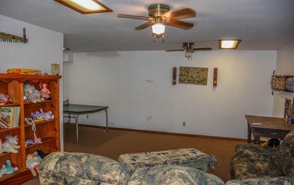 A living room with a ceiling fan, a wooden bookshelf, a table, and a couch. - Kingdom Cabin 1 (Morganton)