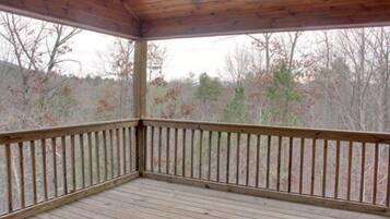 A covered wooden deck with a railing, surrounded by trees.