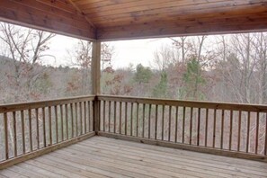 A covered wooden deck with a railing, surrounded by trees.