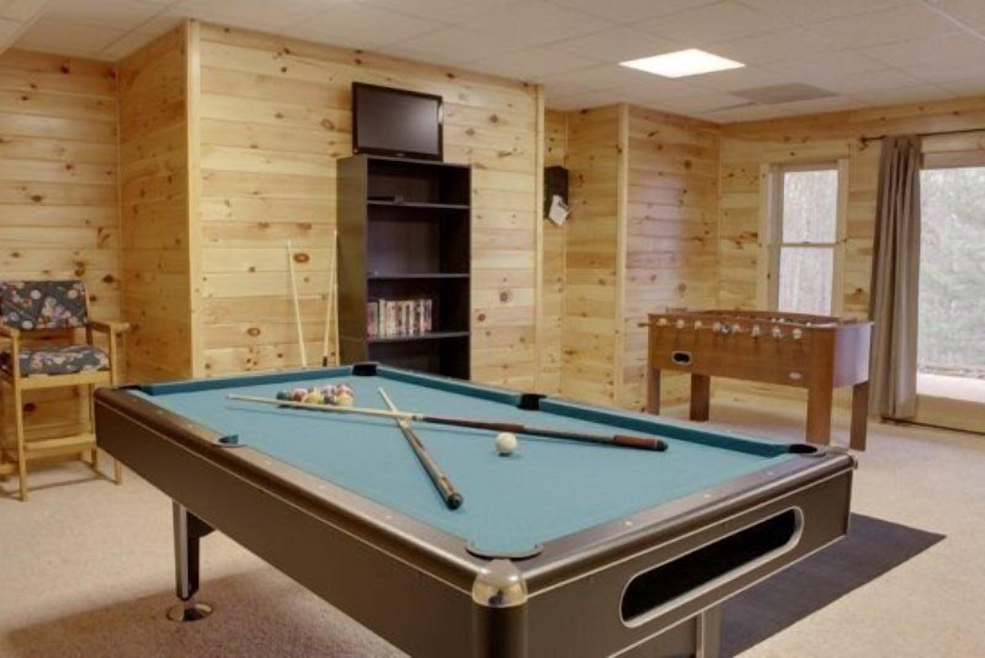 Une table de billard dans une pièce aux murs en bois, avec une table de baby-foot.