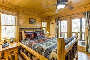 A wooden cabin bedroom with a bed, a nightstand, a lamp, and a ceiling fan.