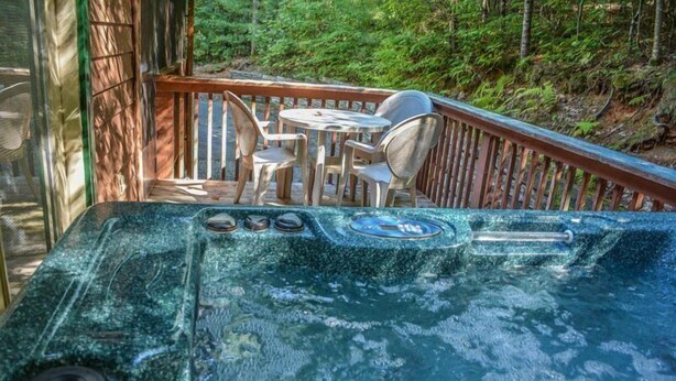 A hot tub with a wooden deck and chairs, surrounded by a forest. - Hackers Hideaway (Blue Ridge)