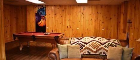 Una habitación con paredes de madera, una mesa de billar y un sofá de cuero con una manta de diseño.