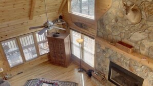 Ein rustikales Blockhaus mit Kamin aus Stein, Holzböden und Deckenventilator.
