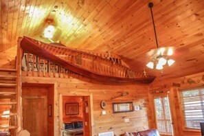 Interior de cabana com escada em formato de barco de madeira, ventilador de teto e janela com persianas.