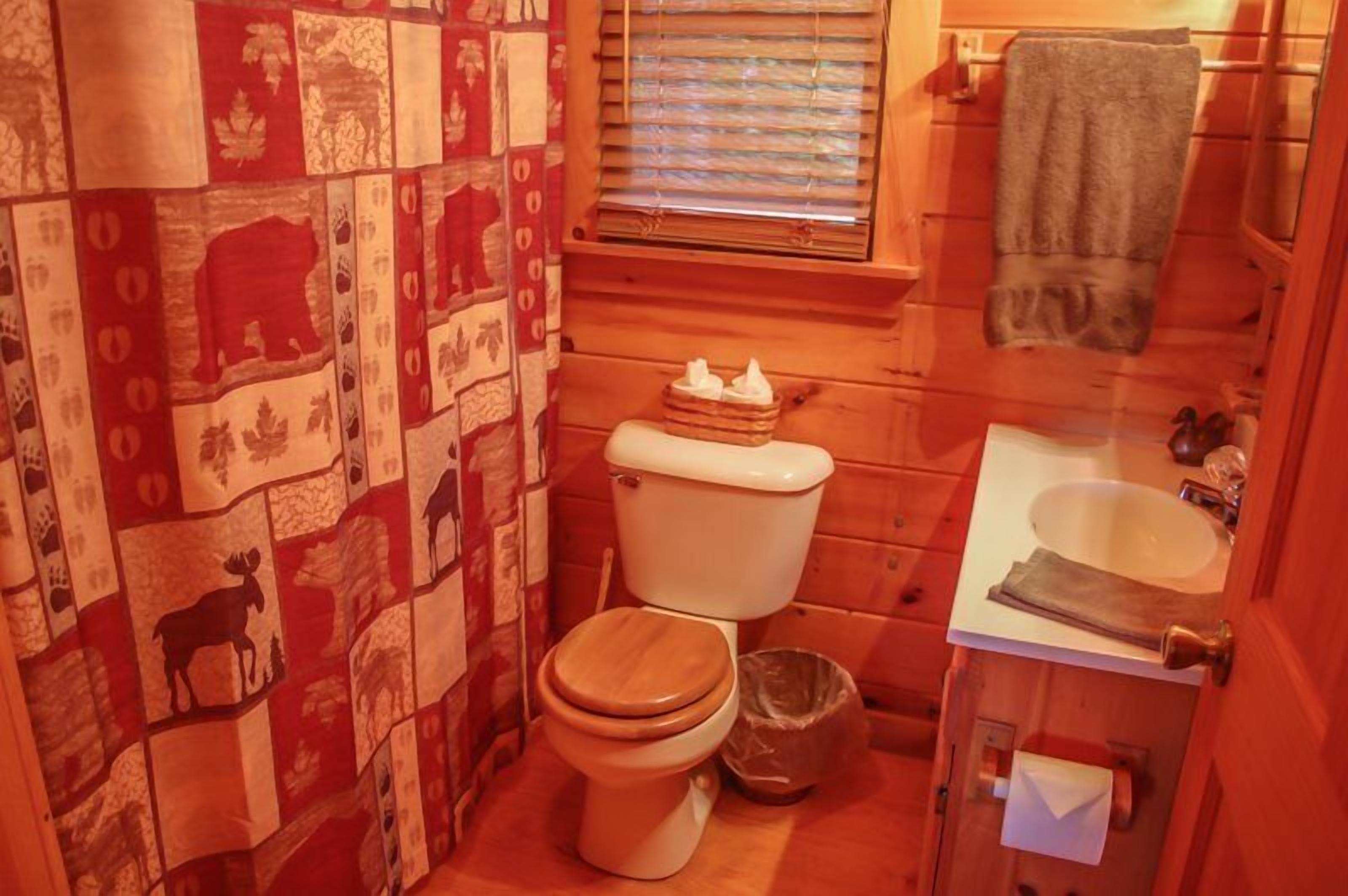 A small, compact bathroom with a wooden floor, a toilet, a sink, and a window with blinds.
