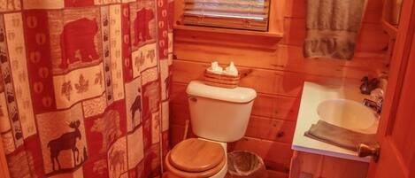 A small, compact bathroom with a wooden floor, a toilet, a sink, and a window with blinds.