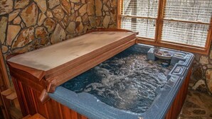 Un bain à remous avec un banc en bois et un mur en pierres en arrière-plan, une fenêtre avec des stores et un sol en pierre.
