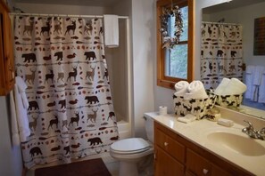 Ein Badezimmer mit Duschvorhang mit Tiermotiven, Toilette, Waschbecken mit Toilettenartikeln und Spiegel.