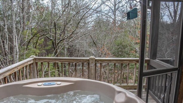 A hot tub on a wooden deck with a glass door, surrounded by trees. - My Mountain Escape (Morganton)