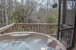 A hot tub on a wooden deck with a glass door, surrounded by trees. - My Mountain Escape (Morganton)