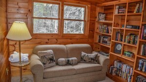 A cozy room with a beige sofa, a lamp, and a bookshelf filled with books. - My Mountain Escape (Morganton)