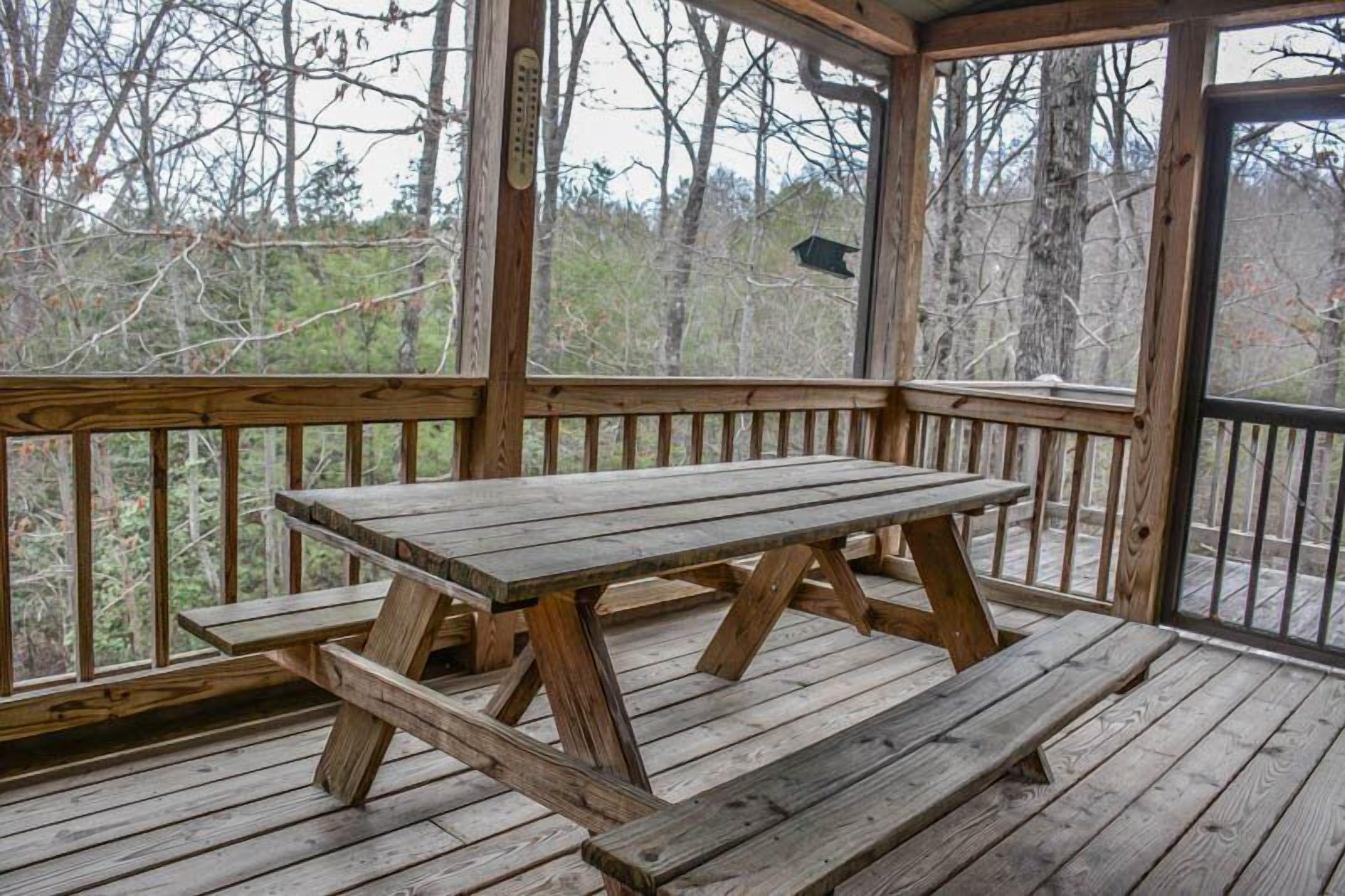 A wooden deck with a picnic table and benches, surrounded by trees.