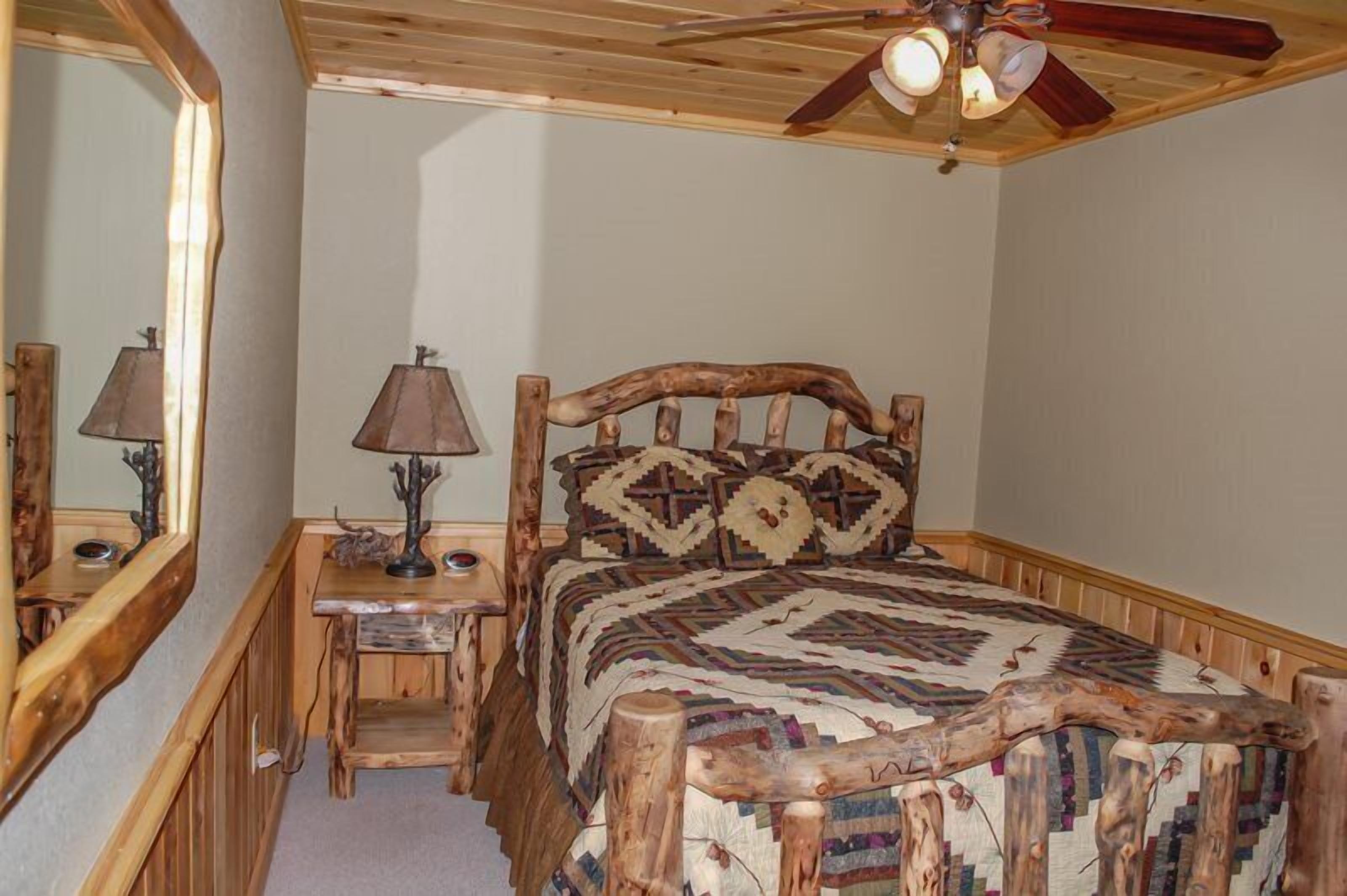 A rustic bedroom with a wooden bed, a nightstand, a lamp, and a ceiling fan.