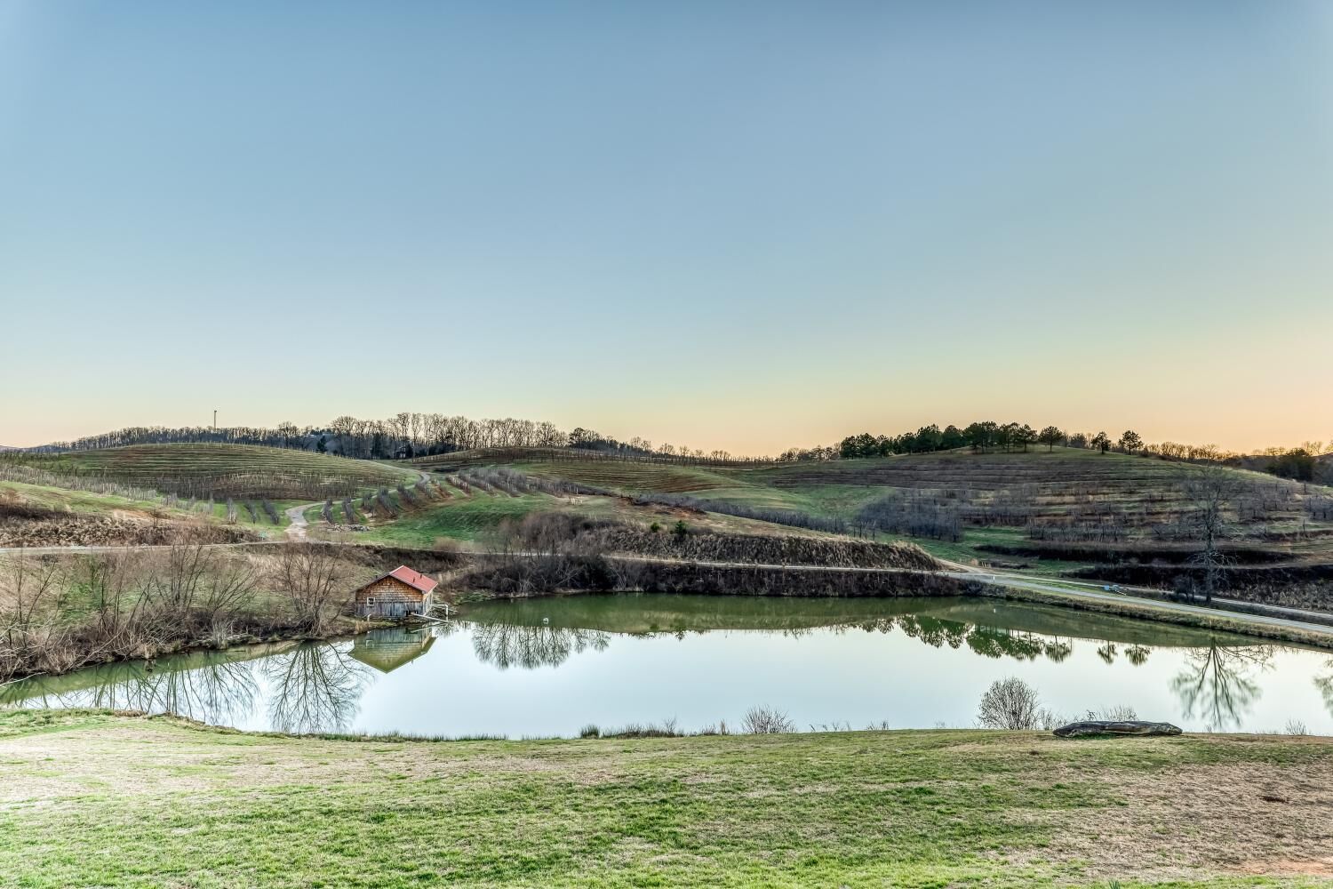 A rural landscape with a pond, a small building, and terraced fields.