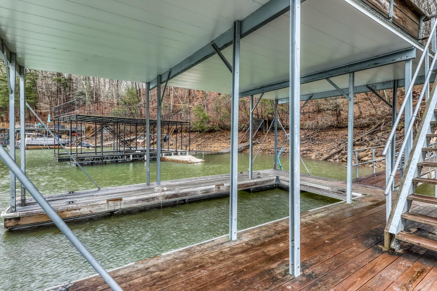 A covered wooden deck with metal railings overlooking a body of water and a dock area.