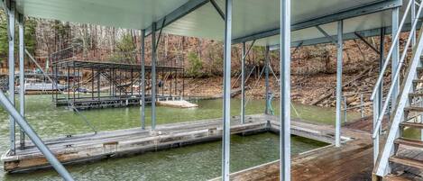 A covered wooden deck with metal railings overlooking a body of water and a dock area.