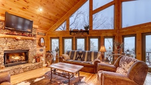 A cozy cabin interior with a stone fireplace, wooden walls, a large window, and a leather sofa. - Lonesome Dove (Blue Ridge)