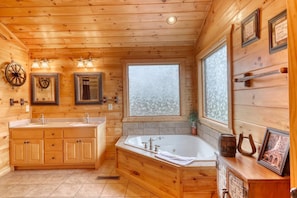 A wooden cabin bathroom with a double sink vanity, a bathtub, and a large frosted window. - Lonesome Dove (Blue Ridge)