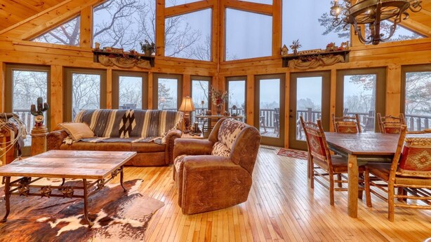 A spacious cabin with a high ceiling, large windows, a cozy seating area with a sofa and chairs, a dining table, and a chandelier. - Lonesome Dove (Blue Ridge)