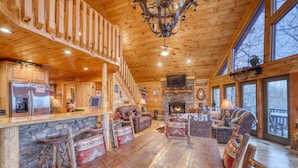 A spacious wooden cabin with a stone fireplace, a dining area with rustic chairs, and a cozy living room with a leather sofa and a television. - Lonesome Dove (Blue Ridge)