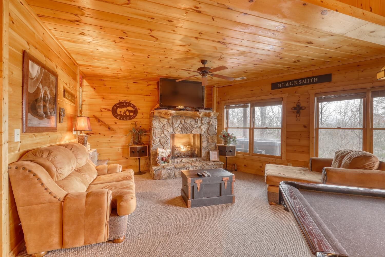 A cozy cabin interior with a stone fireplace, leather sofas, a flat-screen TV, and a sign reading "BLACK SMITH".