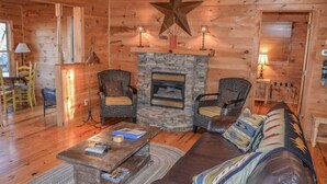 A cozy log cabin interior with a stone fireplace, two wicker armchairs, a sofa, and a coffee table. - Cabin Sweet Cabin (Blue Ridge)
