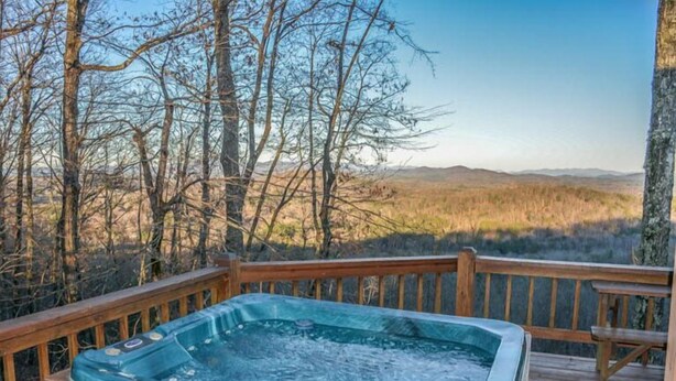 A hot tub on a wooden deck with a view of a forest and distant hills. - Cabin Sweet Cabin (Blue Ridge)