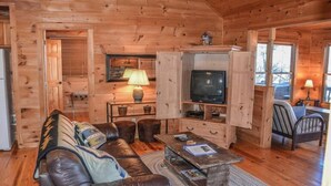 A cozy wooden cabin interior with a leather sofa, a television, and a dining area. - Cabin Sweet Cabin (Blue Ridge)