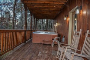 Um deck de madeira com uma banheira de hidromassagem e cadeiras, rodeado por árvores.
