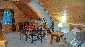 Um quarto de sótão aconchegante com teto de madeira, uma mesa de jantar com cadeiras, um sofá e uma estatueta de girafa.