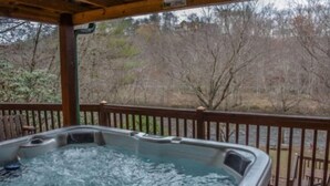 Un jacuzzi con terraza de madera y vista a árboles y un edificio al fondo.