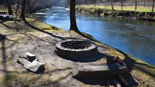Camping junto al río, con un hoyo para la fogata y leña.