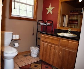 Un baño con inodoro, tocador de madera con lavamanos, decoración con forma de estrella en la pared y ventana con cortinas.