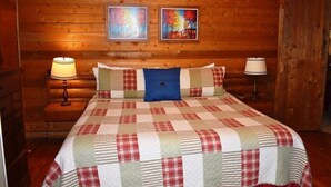 Ein Schlafzimmer einer Holzhütte mit einer gesteppten Bettdecke, zwei gerahmten Bildern an der Wand und zwei Nachttischlampen.