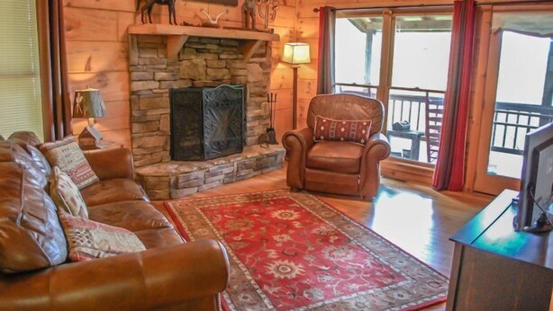 A cozy living room with a stone fireplace, leather sofa, and a red patterned rug. - Into Thin Ayer (Blue Ridge)