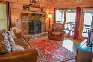 A cozy living room with a stone fireplace, leather sofa, and a red patterned rug. - Into Thin Ayer (Blue Ridge)