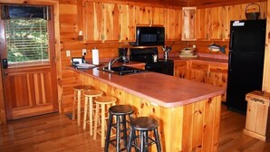 A wooden cabin kitchen with a central island, bar stools, a microwave, and a refrigerator. - Whitetail Lodge (Mineral Bluff)