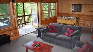 A cozy cabin interior with a grey sofa, a red coffee table, and a foosball table. - Whitetail Lodge (Mineral Bluff)
