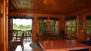 A wooden cabin interior with a dining area, kitchen, and large windows offering a view of the outdoors. - Whitetail Lodge (Mineral Bluff)