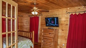 Une chambre dans un chalet en bois, avec un lit, une commode, un téléviseur et des rideaux rouges.