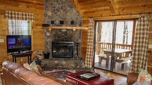 L’intérieur d’un chalet accueillant, avec une cheminée en pierre, un canapé en cuir et un téléviseur.