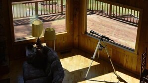 Quarto com grandes janelas que oferecem vista para um campo gramado e um deck de madeira na parte externa.