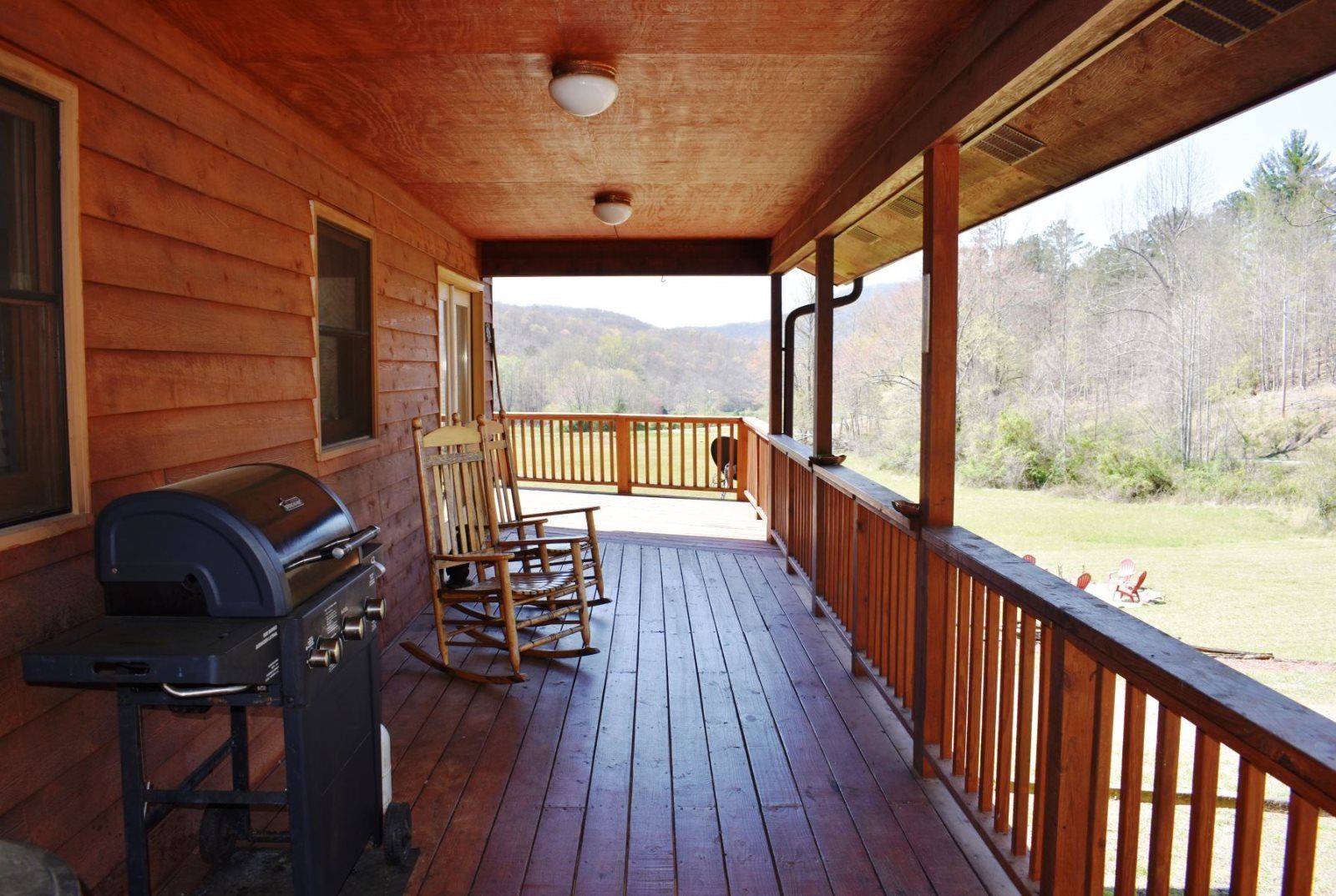 Une cabane en bois avec une véranda, un barbecue et des fauteuils à bascule.