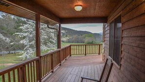 Um deck de madeira com um banco, com vista para uma paisagem pitoresca com árvores e colinas.